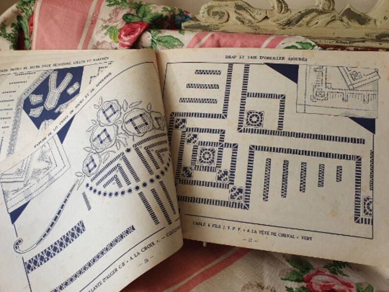 Peut inclure: Un livre de mod&egrave;les de point de croix vintage avec des instructions pour cr&eacute;er une housse de coussin. Le livre pr&eacute;sente un motif bleu et blanc avec un motif floral et un motif g&eacute;om&eacute;trique. Le texte sur la page indique "Drap ST. KT TAIK D'OREILLER AJOURES" et "CABLE & FILS T.P.F. A LA T&Ecirc;TE DE CHEVAL - VERT".