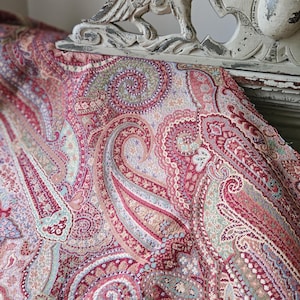 May include: A close-up of a paisley patterned fabric in shades of red, pink, and green. The fabric is draped over a white, distressed decorative piece with a carved bird design. The fabric's intricate design is visible.