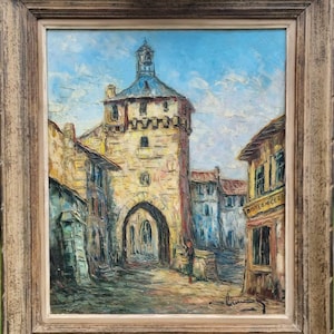 May include: A painting depicting a European town square with a tall stone tower at its centre. The tower features a clock face and a pointed roof. The buildings are painted in warm colours, with a blue sky and white clouds in the background. The painting is framed in a wooden frame.