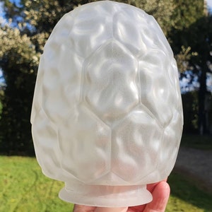 Puede incluir: Pantalla de lámpara de vidrio esmerilado con un patrón geométrico en forma de panal. La pantalla, con forma de huevo, tiene una base ancha y una superficie texturizada. El color es blanco suave y translúcido, y el diseño recuerda al estilo Art Déco.