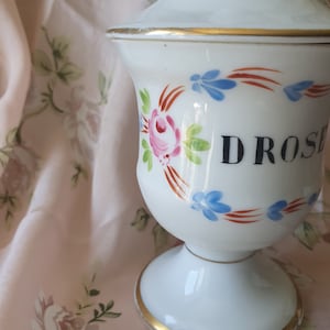 May include: White ceramic jar with a gold trim and a floral design. The jar is labelled "DROSES".