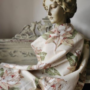Può includere: Un busto classico drappeggiato con un tessuto color crema con un motivo floreale di grandi fiori rosa chiaro e verdi. Il busto è di un colore verde pallido invecchiato e il tessuto è drappeggiato sulle spalle.