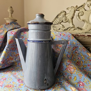 May include: A vintage blue enamel coffee pot with a blue and white trim. The pot has a cone-shaped body and a lid with a small handle.