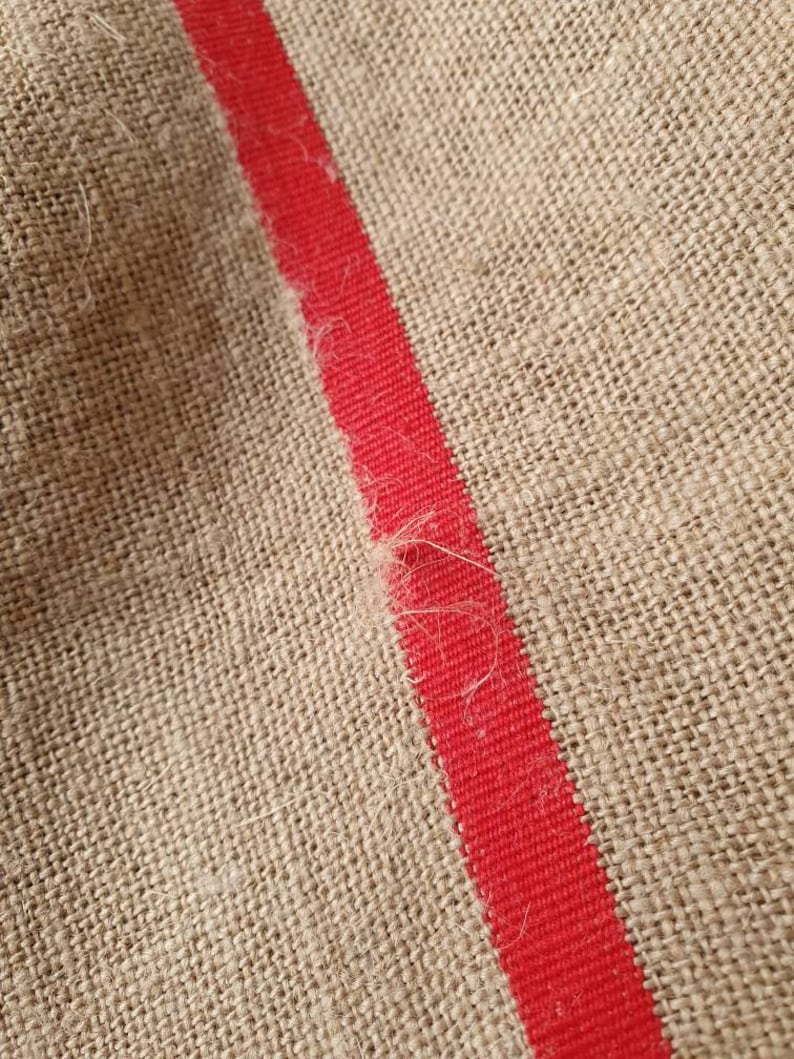 May include: Close-up of a natural burlap fabric with a single red stripe running diagonally across the surface.