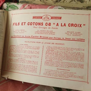 Peut inclure: Un livret vintage de couleur cr&egrave;me avec du texte rouge intitul&eacute; "FILS ET COTONS C-B "A LA CROIX"" pour "Ouvrages de Dames" (travaux pour dames). Le livret comprend des instructions pour le lavage de la broderie et le texte "Les Couleurs des Articles Cartier-Bresson pour Ouvrages de Dames sont solides" (Les couleurs des articles Cartier-Bresson pour les travaux de dames sont solides).