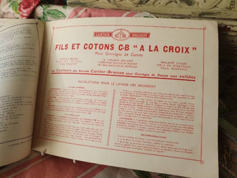 Peut inclure: Un livret vintage de couleur cr&egrave;me avec du texte rouge intitul&eacute; "FILS ET COTONS C-B "A LA CROIX"" pour "Ouvrages de Dames" (travaux pour dames). Le livret comprend des instructions pour le lavage de la broderie et le texte "Les Couleurs des Articles Cartier-Bresson pour Ouvrages de Dames sont solides" (Les couleurs des articles Cartier-Bresson pour les travaux de dames sont solides).