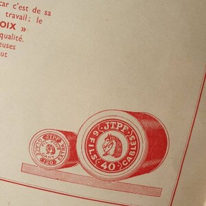 Peut inclure: Deux bobines de fil rouge avec des &eacute;tiquettes blanches. La plus grande bobine porte le texte "9 FILS 40 CABLES JTPF" et un logo de t&ecirc;te de cheval. La plus petite bobine porte le texte "GLA FIL POUR AGANT EXTRA 120".