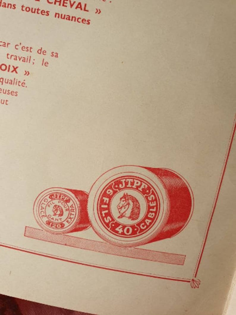 Peut inclure: Deux bobines de fil rouge avec des &eacute;tiquettes blanches. La plus grande bobine porte le texte "9 FILS 40 CABLES JTPF" et un logo de t&ecirc;te de cheval. La plus petite bobine porte le texte "GLA FIL POUR AGANT EXTRA 120".