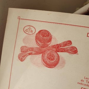 Peut inclure: Un gros plan d'une bobine de fil rouge et blanc avec une croix et les lettres "C.T.B." imprim&eacute;es dessus. La bobine est entour&eacute;e de deux autres bobines de fil.