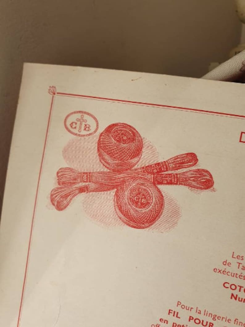 Peut inclure: Un gros plan d'une bobine de fil rouge et blanc avec une croix et les lettres "C.T.B." imprim&eacute;es dessus. La bobine est entour&eacute;e de deux autres bobines de fil.