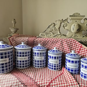 Puede incluir: Conjunto de seis botes de cerámica a cuadros azules y blancos con tapas. Cada bote tiene una etiqueta con una palabra francesa: Sucre, Farine, Café, Pâtes, Chicorée y Poivre. Están colocados sobre un mantel a cuadros rojos y blancos.