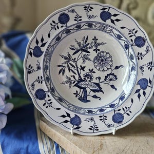 May include: A white ceramic soup bowl with a blue and white floral design. The bowl has a scalloped edge and a raised rim.