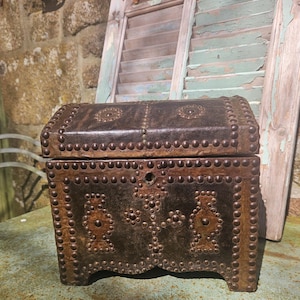 Könnte beinhalten: Eine kleine, dunkelbraune Holzkiste mit einem Lederdeckel. Der Deckel ist mit Metallnieten verziert und hat ein Schlüsselloch. Die Kiste steht auf einer grünen Oberfläche.