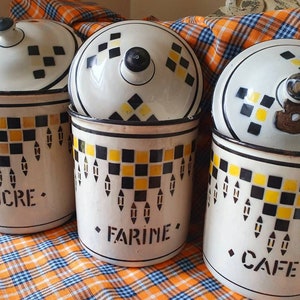 Pode incluir: Três potes de cerâmica vintage com tampas, com um padrão xadrez preto e amarelo. Os potes são etiquetados com "SUCRE", "FARINE" e "CAFÉ".