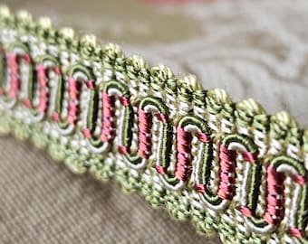 May include: Close-up of a green, white and pink trim with a scalloped edge. The trim is made of woven fabric and has a decorative pattern.