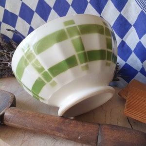 May include: A white ceramic bowl with a green and white checkered pattern. The bowl is sitting on a wooden surface.