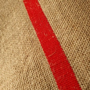 May include: Close-up of a brown burlap fabric with a thick red stripe running diagonally across the surface.