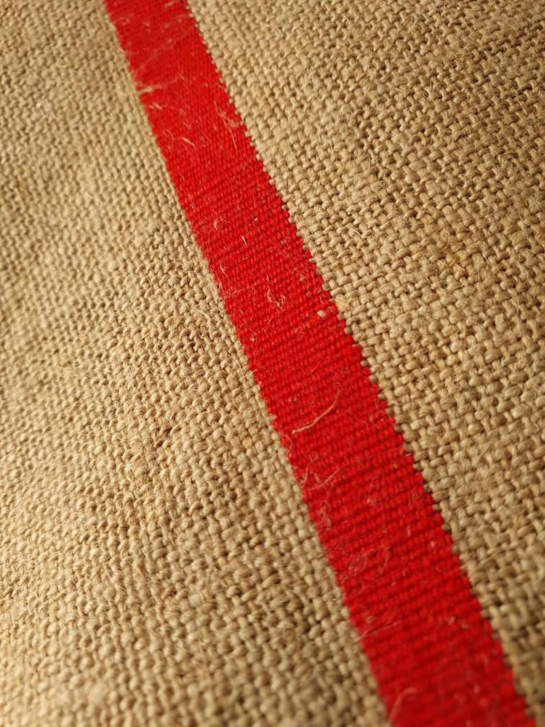 May include: Close-up of a brown burlap fabric with a thick red stripe running diagonally across the surface.