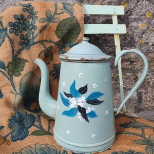 May include: A light blue enamel coffee pot with a floral design featuring blue leaves and white flowers. The pot has a handle and a spout.