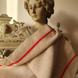 May include: A beige linen throw blanket with two red stripes. The blanket is draped over a plaster bust of a woman.