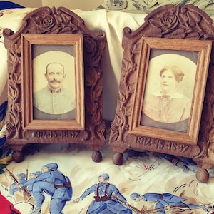 May include: Two antique wooden picture frames with carved floral details. Each frame holds a black and white photograph of a person. The frames are dated "1914-15-16-17".