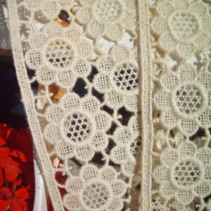 Puede incluir: Borde de encaje blanco con un delicado diseño floral. El encaje está hecho de un material fino y ligero y tiene una textura suave y fluida.