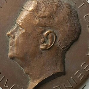 Puede incluir: Una medalla de bronce con un retrato de perfil de un hombre. La medalla tiene el texto "AMERIQUE" y "SEINE" alrededor del borde.