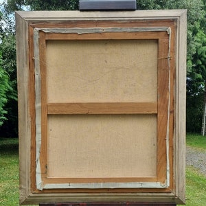 May include: The back of a framed canvas painting. The canvas is stretched over a wooden frame and is secured with staples. The frame is made of wood and is painted a light brown colour. The painting is in a light wood frame.