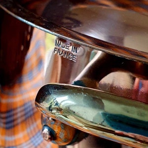 May include: Close-up of a silver pot with a shiny, reflective surface. The pot has a handle and a lid. The lid has the words "Made in France" engraved on it.
