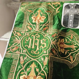 May include: Green velvet liturgical textile with gold embroidery. The design includes floral motifs, geometric borders, and the letters IHS. A printed image of a cross is visible in the upper right corner. The textile is likely used for religious ceremonies.