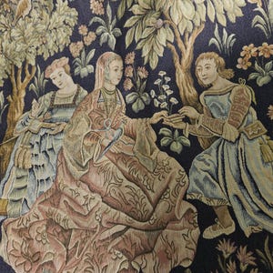 May include: A woven tapestry featuring a dark blue background with a scene of three figures in historical attire. A central figure sits holding a bird, flanked by two other figures amidst stylized trees, flowers, and foliage in shades of gold, green, and cream.