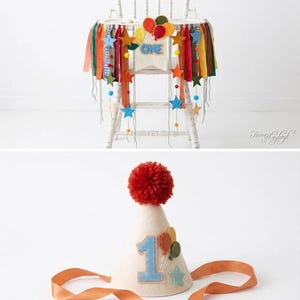 May include: A white high chair decorated with a colorful fabric banner featuring felt stars, balloons, and the word ONE, paired with a matching cone-shaped party hat topped with a red yarn pom-pom and featuring a blue number one and balloons.