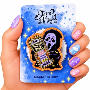 May include: A magnetic grip featuring a black ghost-like figure holding a Fright Night movie ticket with orange glitter borders. The ticket displays text including Fright Night, October Admission, Screen 13, 7:00 PM, and Ticket. The backing card is blue.