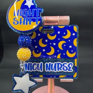 May include: A badge reel with a blue and yellow moon and star design, with the words "NIGHT SHIFT" and "NICU NURSE" in white. The badge reel has blue and yellow beaded accents and a white star charm.