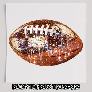 May include: A football with a glittery, sequined design in shades of copper and gold. The football has white laces and is set against a white background. The text "READY TO PRESS TRANSFERS" is at the bottom.