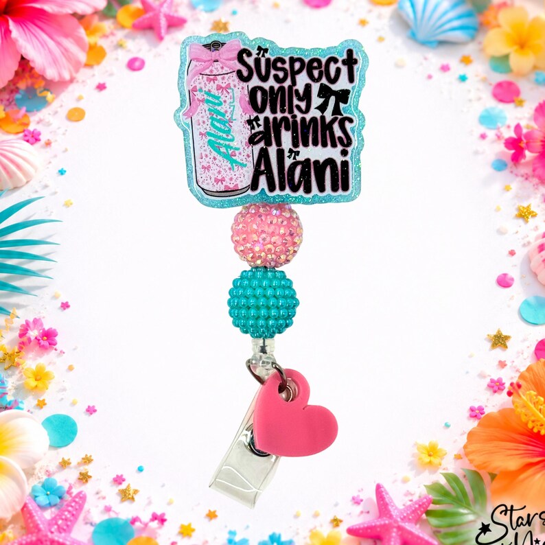 May include: A badge reel featuring a glittery light blue acrylic topper with the text Suspect only drinks Alani, a pink bow, and a can graphic. Below are two textured beads in pink and teal, followed by a solid pink heart charm and a metal clip.