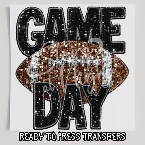 May include: A black and brown iron-on transfer with the text "GAME DAY" and a football in the center. The text and football are decorated with silver glitter.