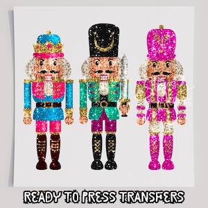 May include: Three glitter-effect nutcracker designs in vibrant colours. One is blue and pink, another teal and purple, and the third pink and gold. The text "READY TO PRESS TRANSFERS" is at the bottom of the image.