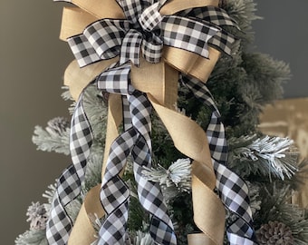 May include: A decorative Christmas tree bow featuring a combination of black and white checkered ribbon and natural burlap ribbon. The bow is placed on a flocked Christmas tree, creating a festive holiday decoration.
