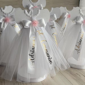 May include: White tulle and satin dresses with gold lettering that says "1st Communion" and "Aldriana's 1st Communion".
