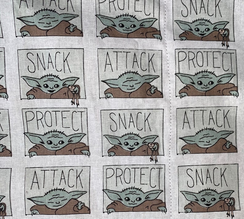 Pu&ograve; includere: Tessuto bianco con un motivo ripetuto di un personaggio dei cartoni animati in una veste marrone. Ogni personaggio &egrave; incorniciato in un riquadro grigio con le parole "SNACK", "ATTACK" e "PROTECT" in testo nero. Il personaggio tiene in mano una piccola creatura.