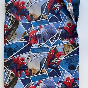 Puede incluir: Un art&iacute;culo de tela azul con un patr&oacute;n repetido de Spider-Man en poses de acci&oacute;n. El dise&ntilde;o incorpora paisajes urbanos y formas geom&eacute;tricas en tonos de azul, rojo y blanco. Tambi&eacute;n es visible una silueta de ara&ntilde;a negra.