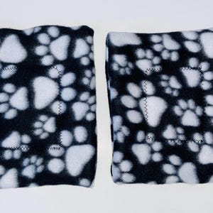 May include: Two black fleece knee pads with a white paw print pattern.