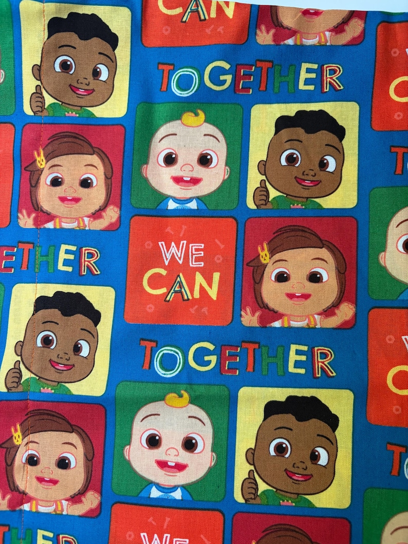May include: A blue fabric featuring a repeating pattern of cartoon characters in square frames of red, yellow, and green. The text WE CAN TOGETHER is printed in yellow and green letters throughout the design, interspersed with the character faces.