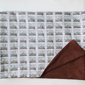 Pu&ograve; includere: Una coperta reversibile con un motivo ripetuto di un personaggio dei cartoni animati e le parole "ATTACK", "PROTECT" e "SNACK". Un lato &egrave; bianco a fantasia, l'altro &egrave; marrone tinta unita. Adatta per letto o divano.