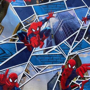 Puede incluir: Tela con un patr&oacute;n repetido de Spider-Man en poses de acci&oacute;n. El dise&ntilde;o incorpora un tel&oacute;n de fondo de paisaje urbano con formas geom&eacute;tricas azules, rojas y blancas, creando una est&eacute;tica din&aacute;mica de c&oacute;mic.