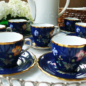 May include: A set of blue and gold teacups and saucers with floral designs. The cups and saucers are arranged on a silver tray.