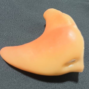 May include: A bright orange and yellow plastic fake nose prop. The nose is shaped like a curved, pointed beak.