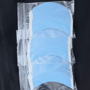 May include: A clear plastic bag containing three stacks of light blue tape. The tape is in the shape of a curved line and is designed for attaching hair extensions.