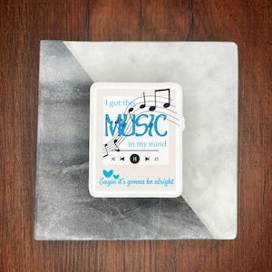 May include: White sticker with black musical notes and the text "I got this MUSIC in my mind" with a play button and two blue hearts below the text. The text below the play button says "Sayin' it's gonna be alright."